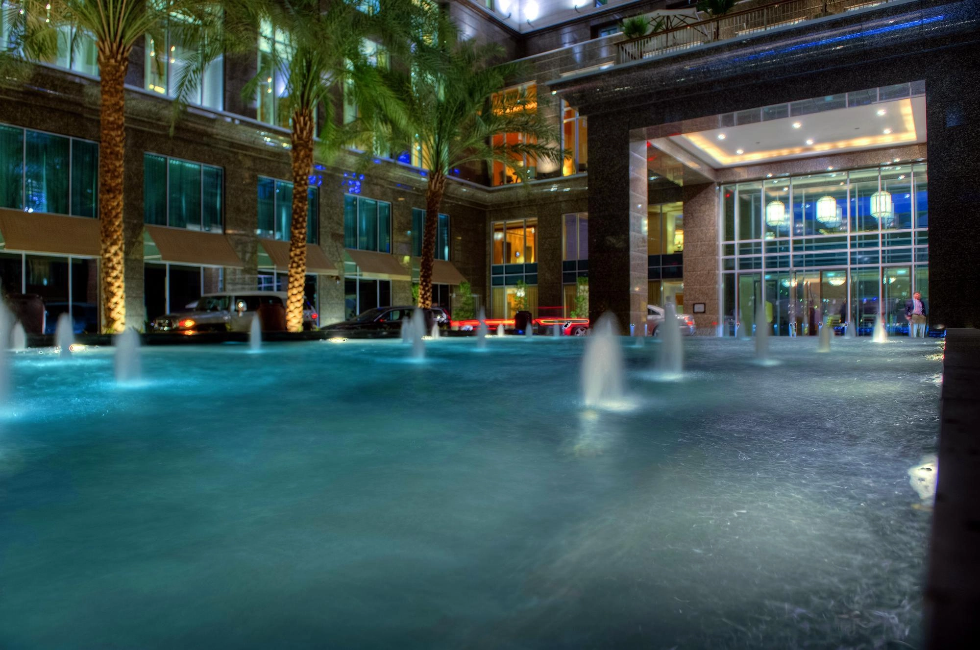 Une grande fontaine lumineuse devant un bâtiment moderne avec des palmiers la nuit.