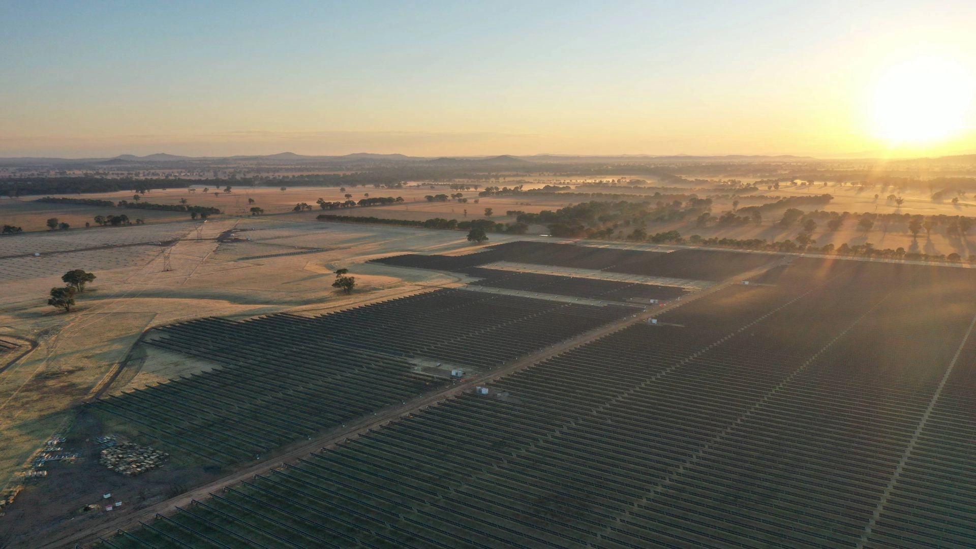 Vue aérienne d'un vaste parc solaire au lever du soleil, avec de longues ombres sur un paysage rural brumeux.