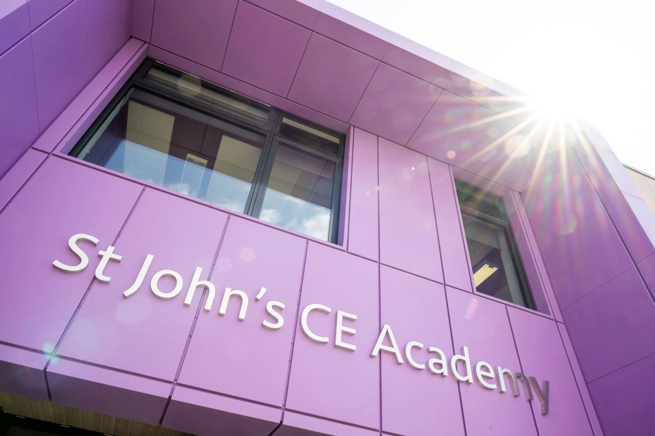 Façade violette moderne de la St John's CE Academy sous un soleil éclatant avec reflet.