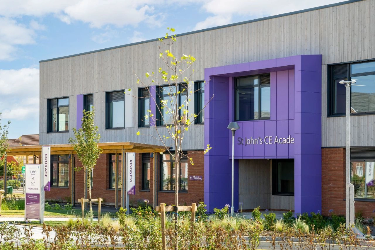 Bâtiment scolaire moderne avec une entrée violette et des panneaux prônant le courage et la bienveillance.