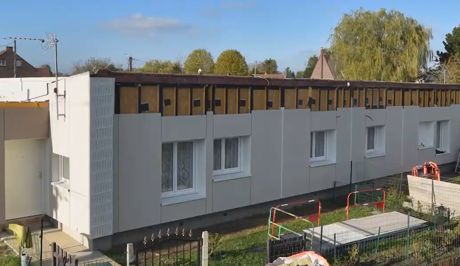 Maisons individuelles en cours de rénovation avec isolation thermique par l'extérieur, montrant les panneaux d'isolation et le nouveau bardage gris clair avec des fenêtres.
