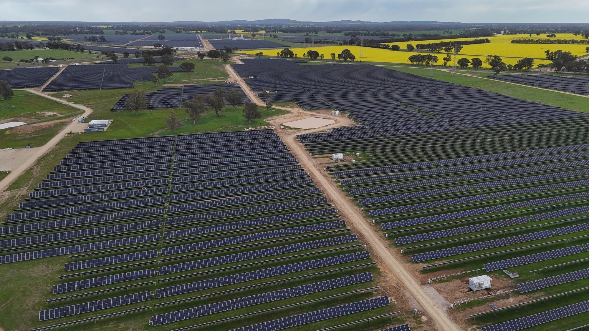 Grand parc solaire avec des rangées de panneaux photovoltaïques dans une campagne verdoyante et des champs de colza.