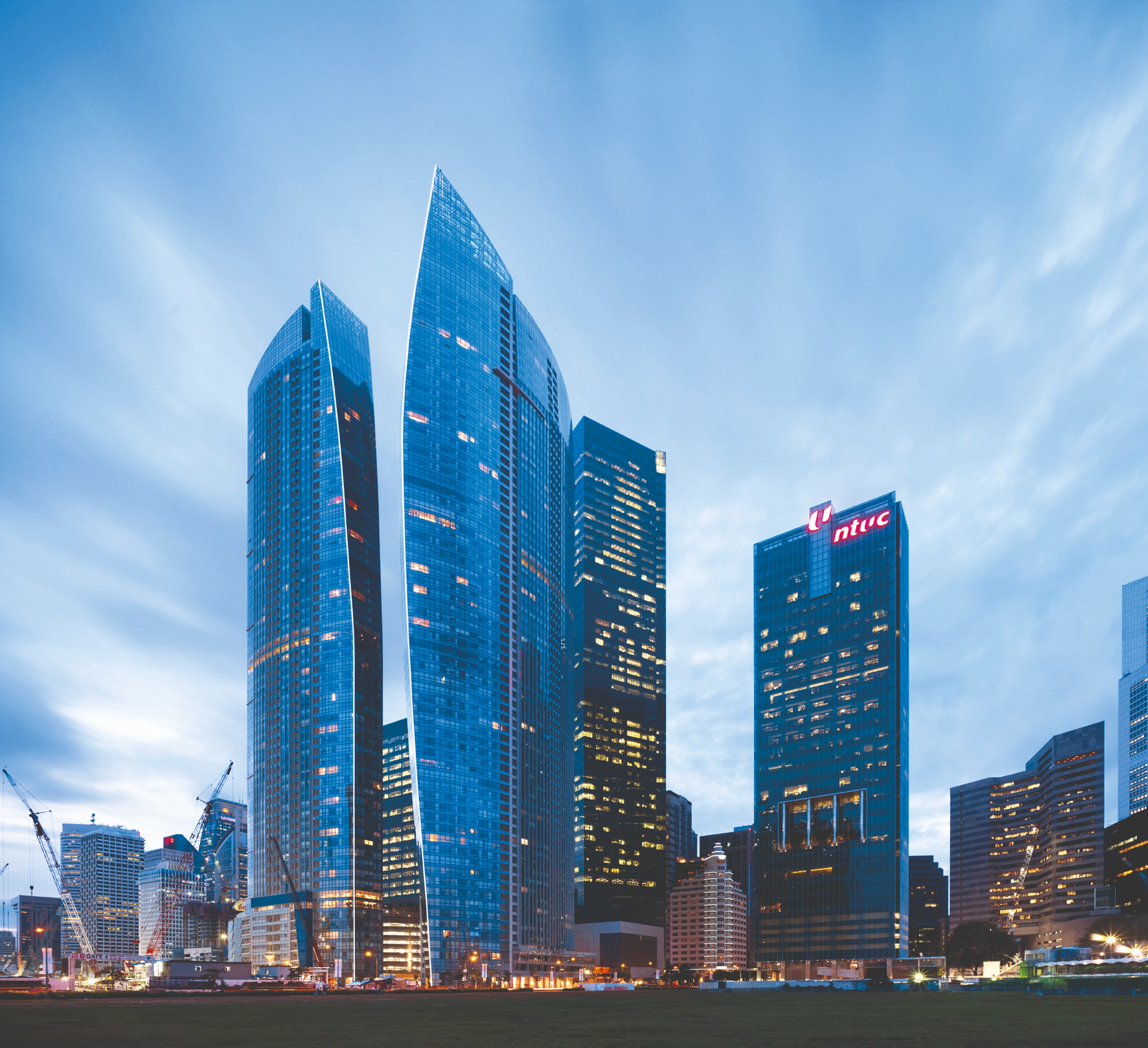 Des gratte-ciel modernes à Singapour s'illuminent sous un ciel crépusculaire au-dessus d'un terrain verdoyant.