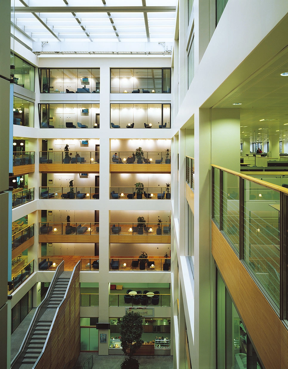 Atrium moderne d'un immeuble de bureaux avec parois vitrées, balcons, escalier et verrière.