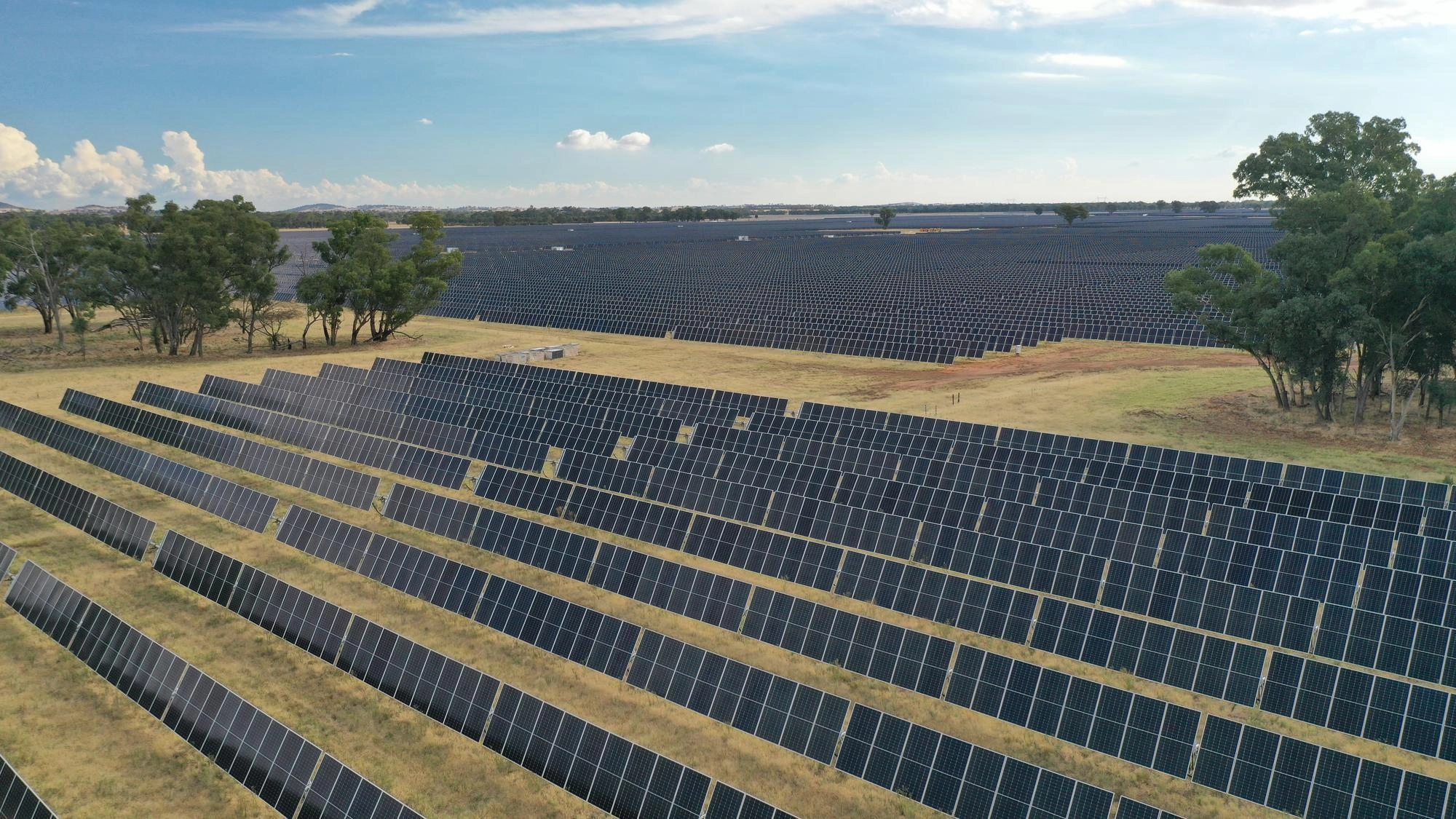 Vaste ferme solaire avec des rangées de panneaux dans un paysage rural sous un ciel clair.