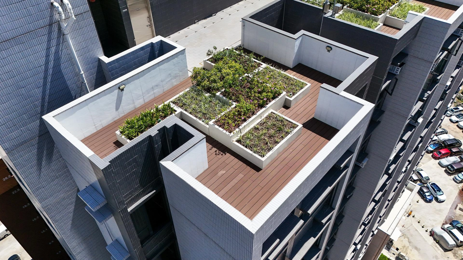 Jardin sur le toit avec terrasse en bois et jardinières rectangulaires sur un immeuble moderne carrelé.