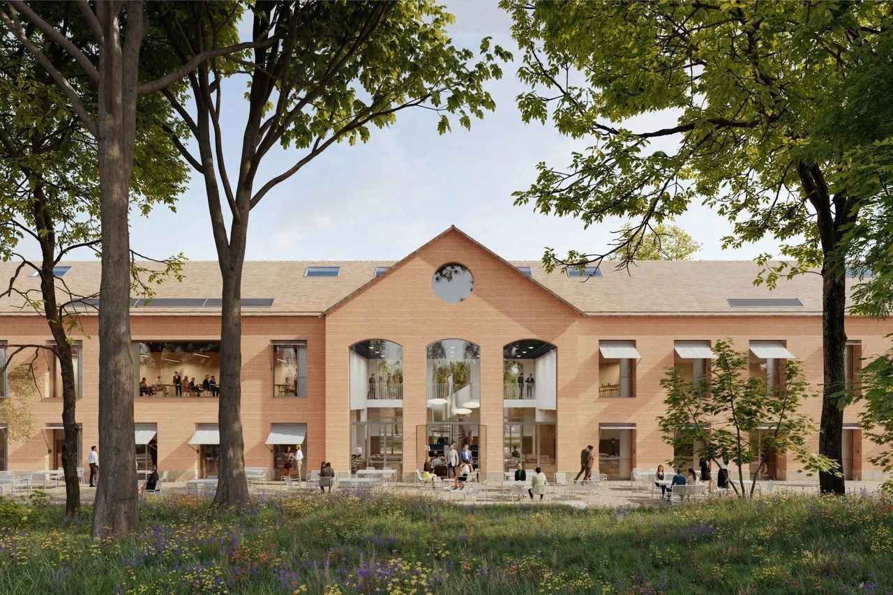 Grand bâtiment moderne en briques orange avec un toit clair, de larges fenêtres et un fronton central orné d'une fenêtre ronde. Des personnes sont assises sur une terrasse extérieure meublée de tables blanches, devant un jardin fleuri et encadré par de grands arbres.