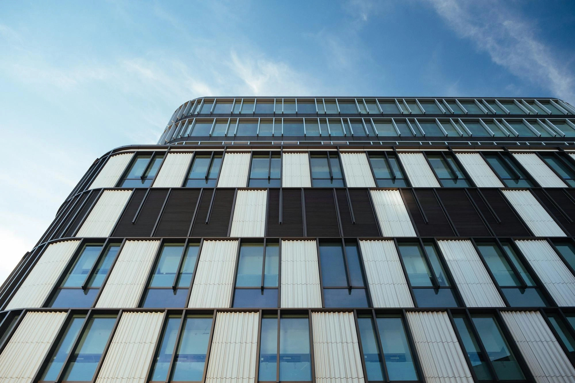 Vue en contre-plongée d'une façade de bureau moderne avec un motif géométrique de fenêtres sous un ciel bleu.