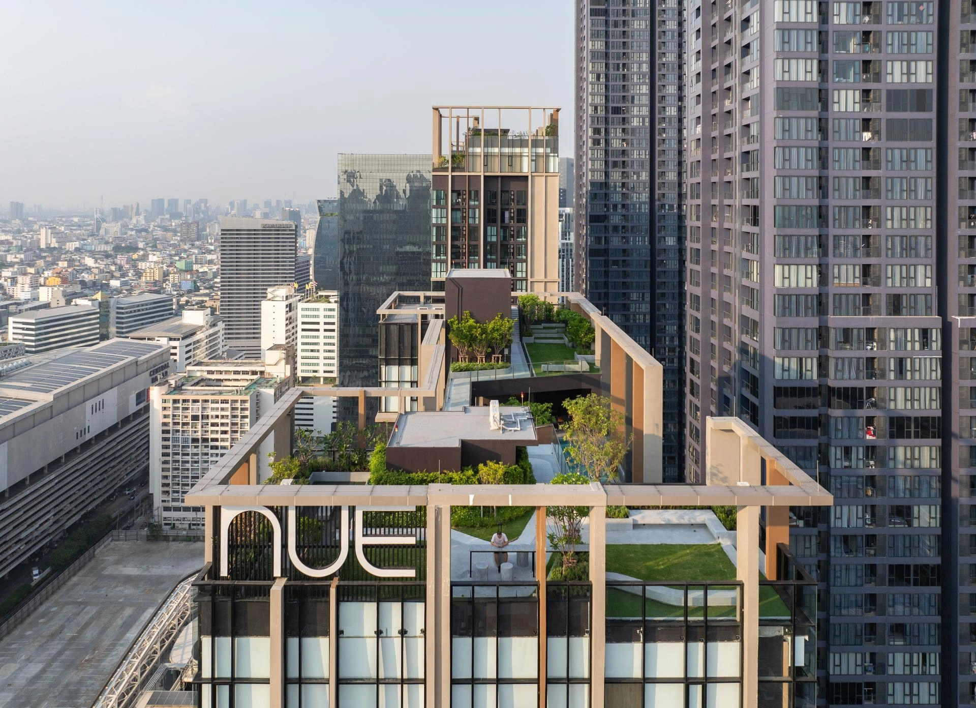 Toit d'un gratte-ciel moderne avec terrasses verdoyantes et enseigne 'NUE', surplombant un paysage urbain.