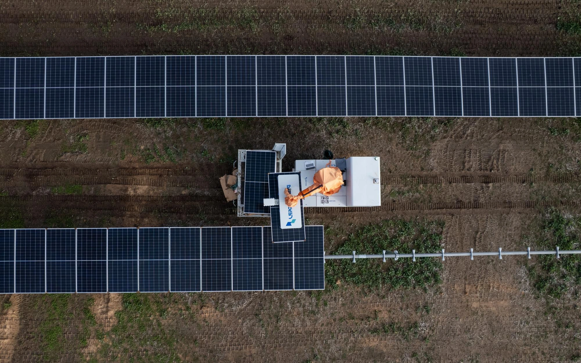 Vue aérienne d'un robot installant des panneaux solaires dans un champ entre deux longues rangées.