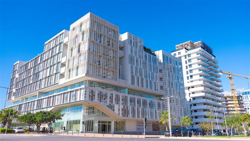 Immeubles blancs modernes aux façades vitrées sous un ciel bleu éclatant dans un décor urbain ensoleillé.