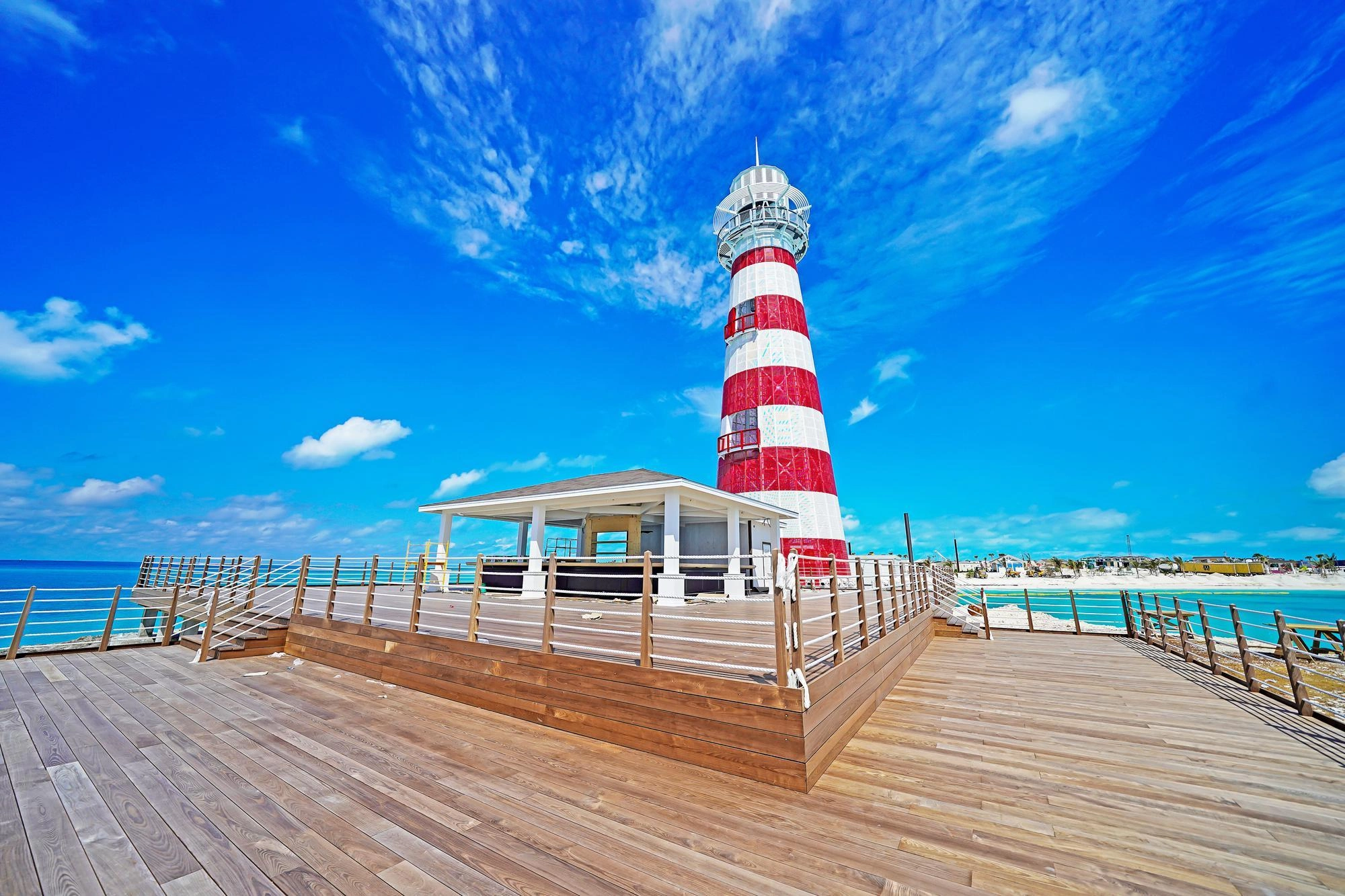 Un phare rayé rouge et blanc à côté d'un ponton en bois et d'un pavillon blanc sous un ciel bleu radieux.