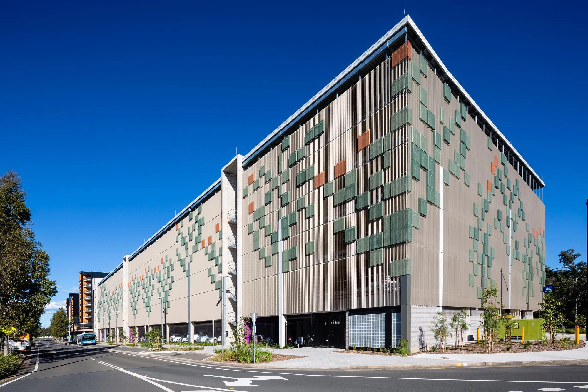 Parking moderne à plusieurs niveaux avec façade décorative verte et ciel bleu éclatant.