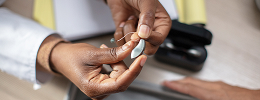 Image of hearing care professional's hands holding a standard hearing aid and showing to a patient